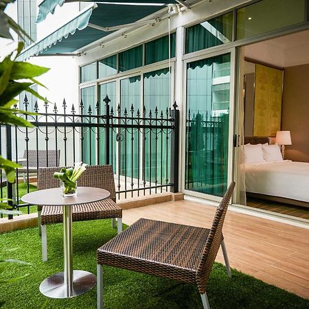 Hotel Dorsett Putrajaya Exteriér fotografie The photo shows a small outdoor balcony or terrace area featuring two wicker-style chairs and a round table. The floor is covered with artificial grass, creating a cozy and inviting atmosphere. In the background, there is a glass wall that leads into