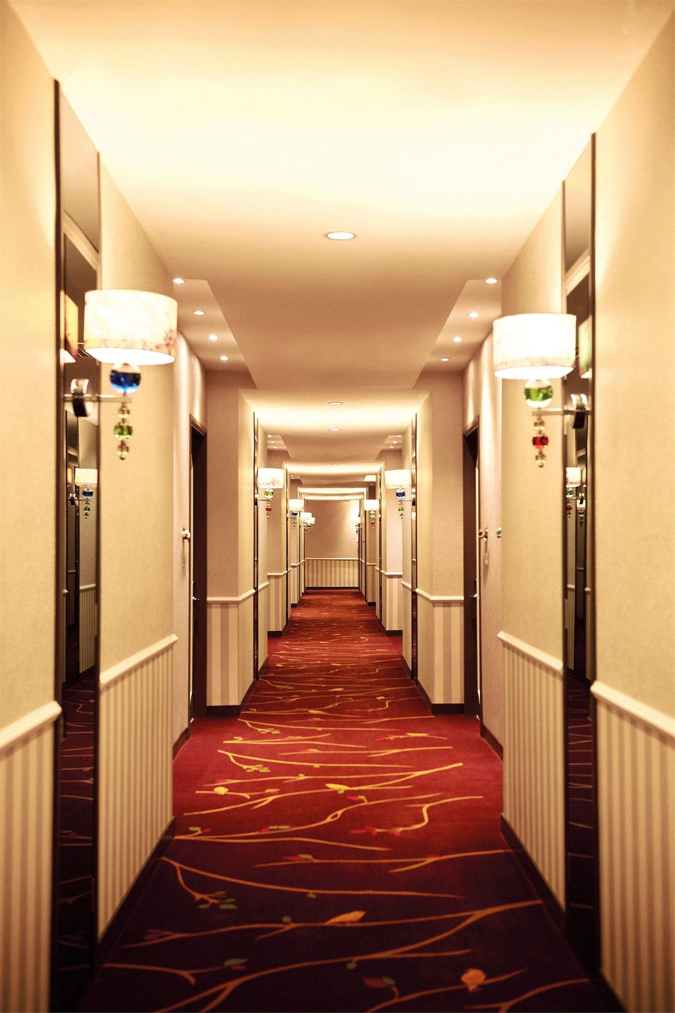 Hotel Dorsett Putrajaya Exteriér fotografie The photo shows a hotel corridor with a long perspective. The walls are painted in a light color, and the floor is covered with a red carpet featuring stylized patterns. There are several closed doors along both sides of the hallway, likely leading t