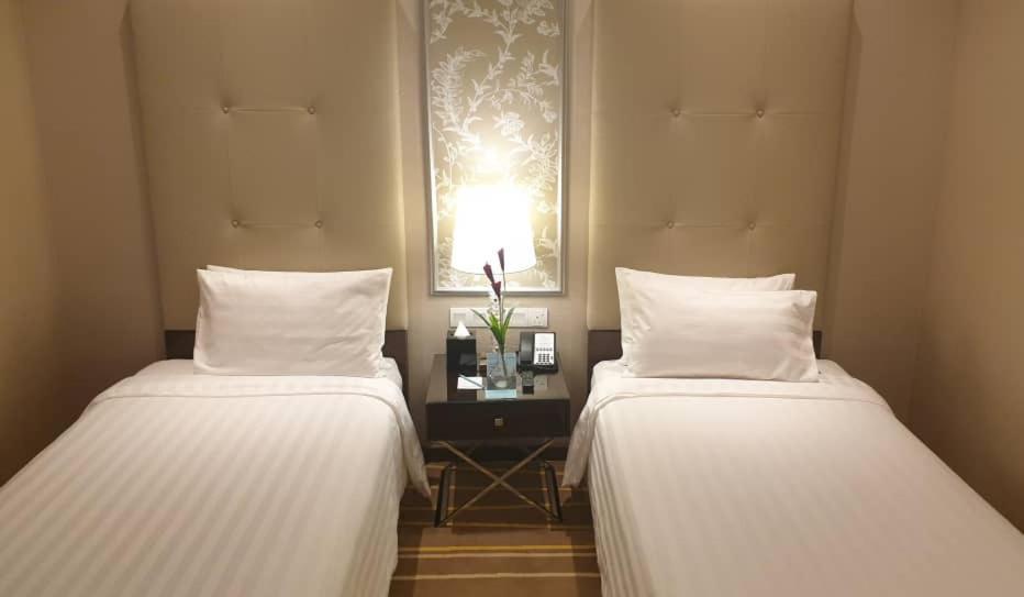 Hotel Dorsett Putrajaya Exteriér fotografie The photo shows a cozy hotel room featuring two twin beds with white bedding. Each bed has a neatly arranged white pillow. Between the beds is a small bedside table, which holds a lamp, a couple of decorative plants, and some electronic devices. The 