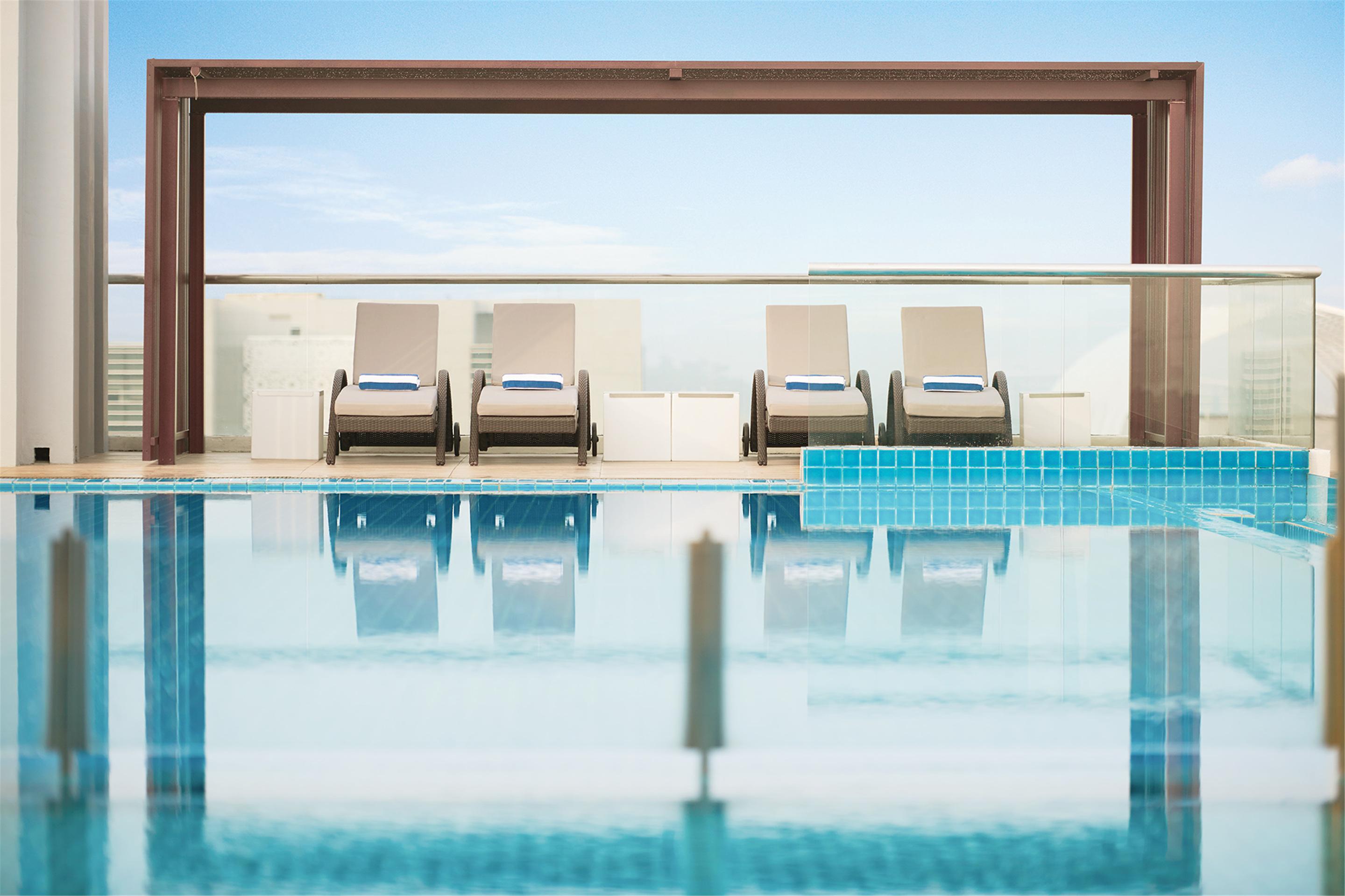 Hotel Dorsett Putrajaya Exteriér fotografie The photo shows a serene pool area featuring a swimming pool with clear blue water. Alongside the pool, there are four lounge chairs arranged neatly, each with a towel placed on them. The background includes a glass railing, allowing for an unobstruc