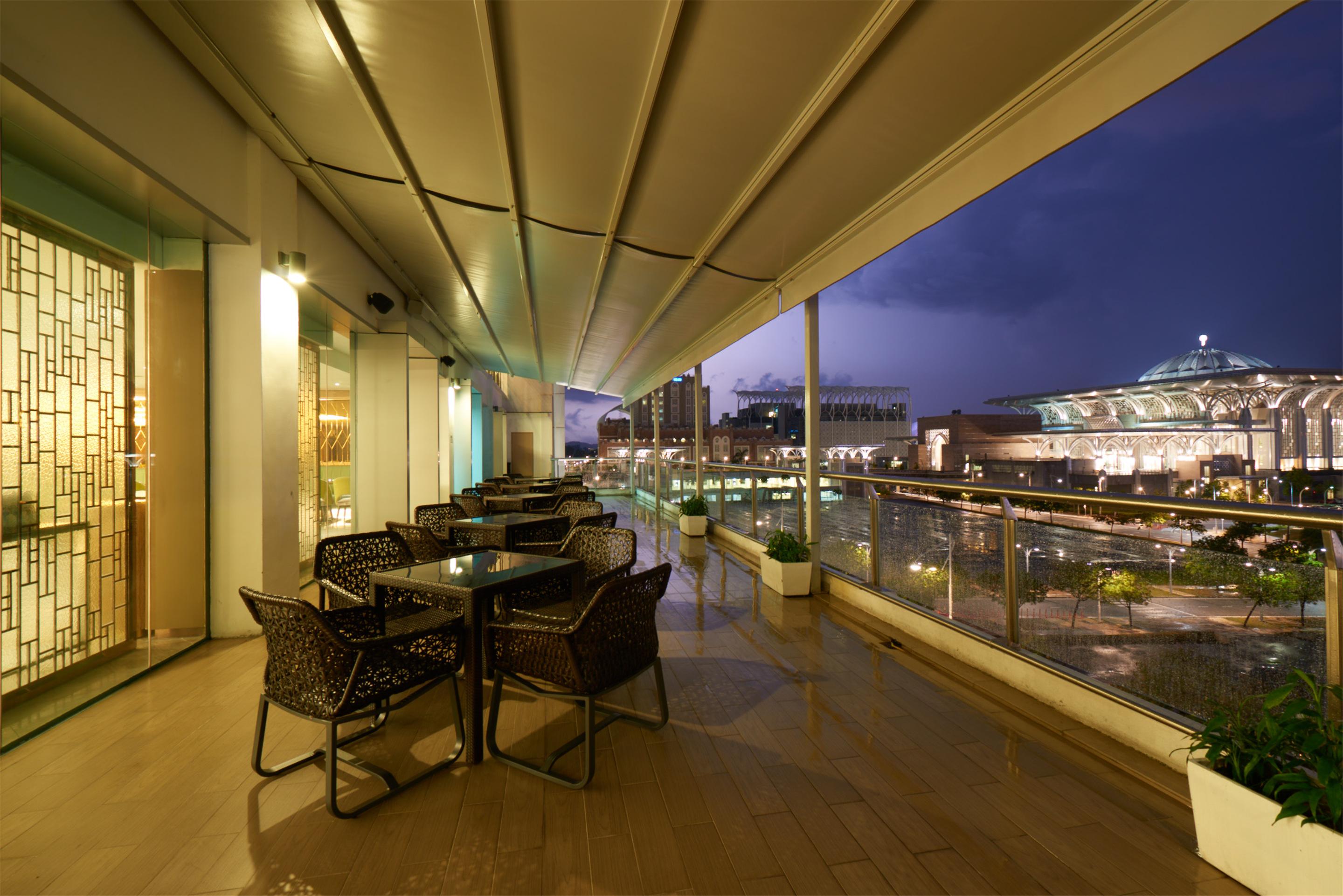 Hotel Dorsett Putrajaya Exteriér fotografie The photo shows a modern outdoor terrace or balcony area with a sleek design. It features several tables surrounded by wicker chairs, suggesting a setting for dining or relaxation. The flooring appears to be polished, and the area is partially covere