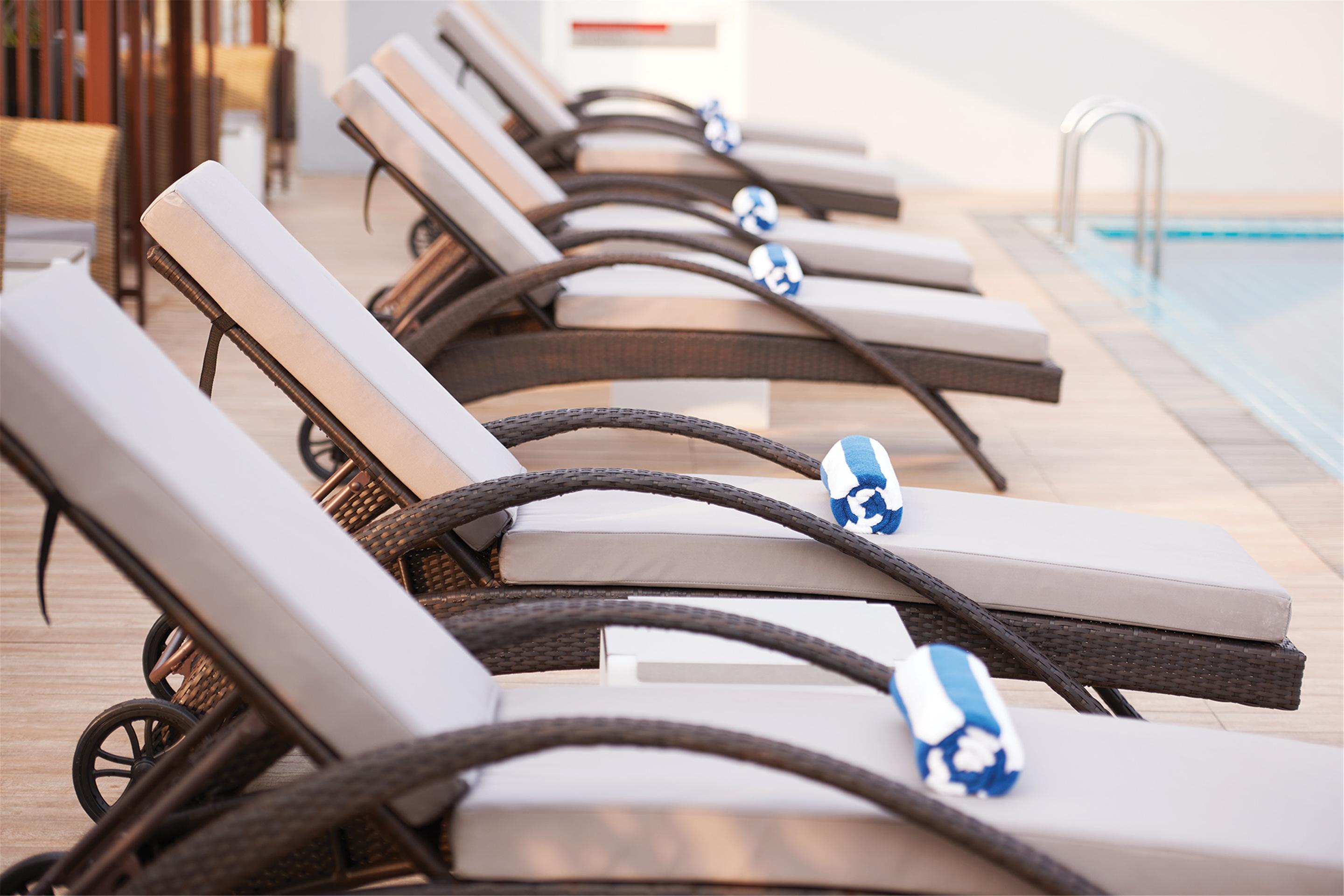 Hotel Dorsett Putrajaya Exteriér fotografie The photo shows a row of reclined lounge chairs that are lined up next to a swimming pool. Each chair has a light-colored cushion and is accompanied by a blue and white rolled towel placed on the seat. The setting appears to be a sunny, relaxing area