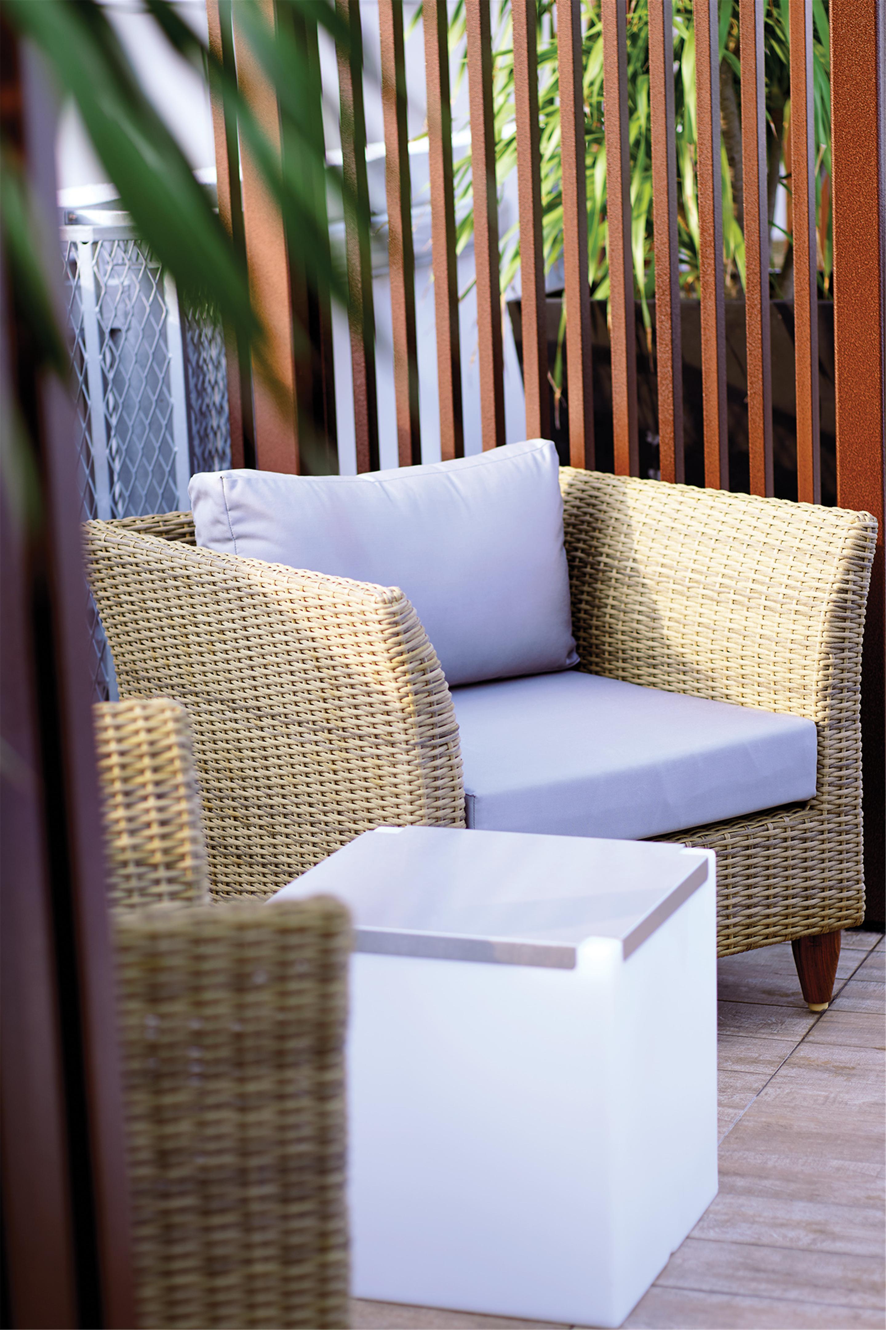 Hotel Dorsett Putrajaya Exteriér fotografie The photo shows a cozy seating area featuring a wicker chair with a light cushion placed on the seat. The chair is part of a patio or outdoor setting, and there is a small, white side table next to it. The background includes wooden slats, suggesting