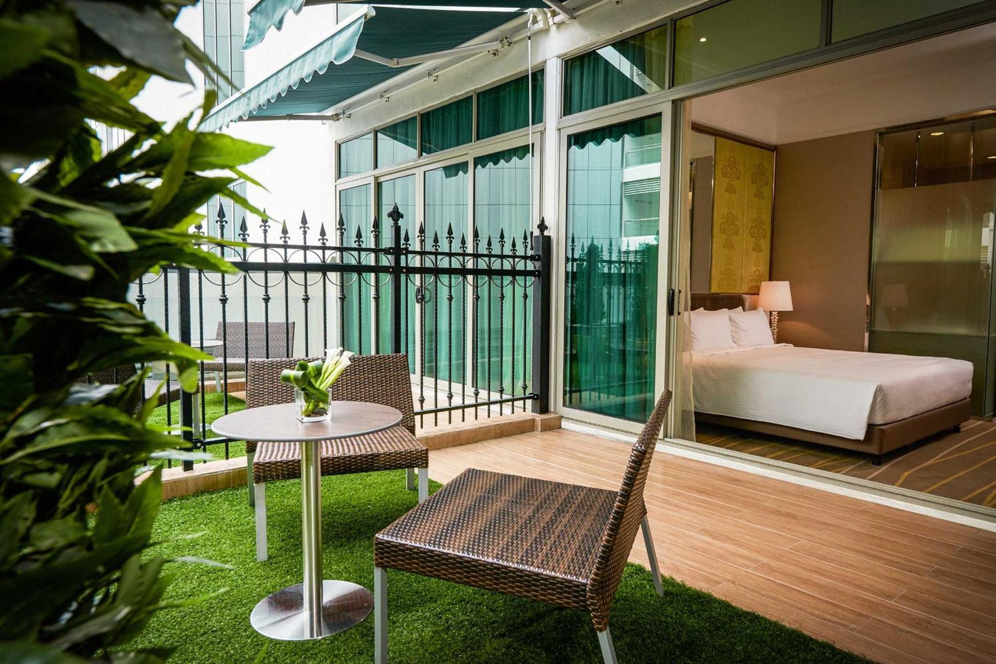 Hotel Dorsett Putrajaya Exteriér fotografie The photo shows a small outdoor balcony or terrace area featuring two wicker-style chairs and a round table. The floor is covered with artificial grass, creating a cozy and inviting atmosphere. In the background, there is a glass wall that leads into