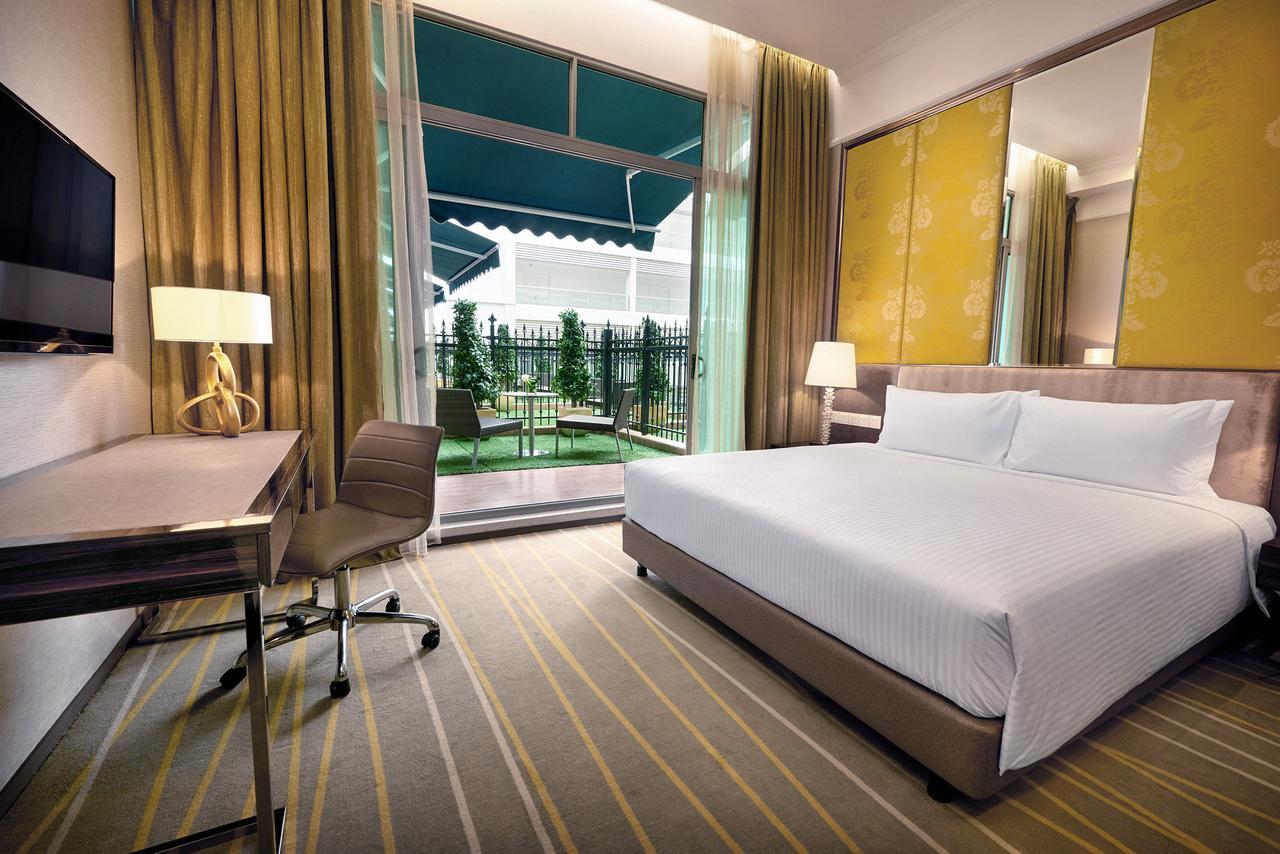 Hotel Dorsett Putrajaya Pokoj fotografie The photo shows a modern hotel room featuring a comfortable king-sized bed with crisp white bedding. Alongside the bed, there is a small nightstand with a lamp. A dedicated workspace includes a desk and an ergonomic chair. Large windows are draped wi