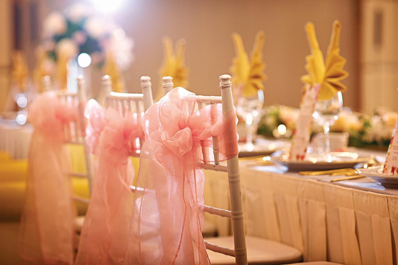 Hotel Dorsett Putrajaya Exteriér fotografie The photo depicts a beautifully arranged dining setup, likely for a special event like a wedding or celebration. Wooden chairs, adorned with soft pink sashes, are lined up, creating an elegant atmosphere. The table is set with white tablecloths and f