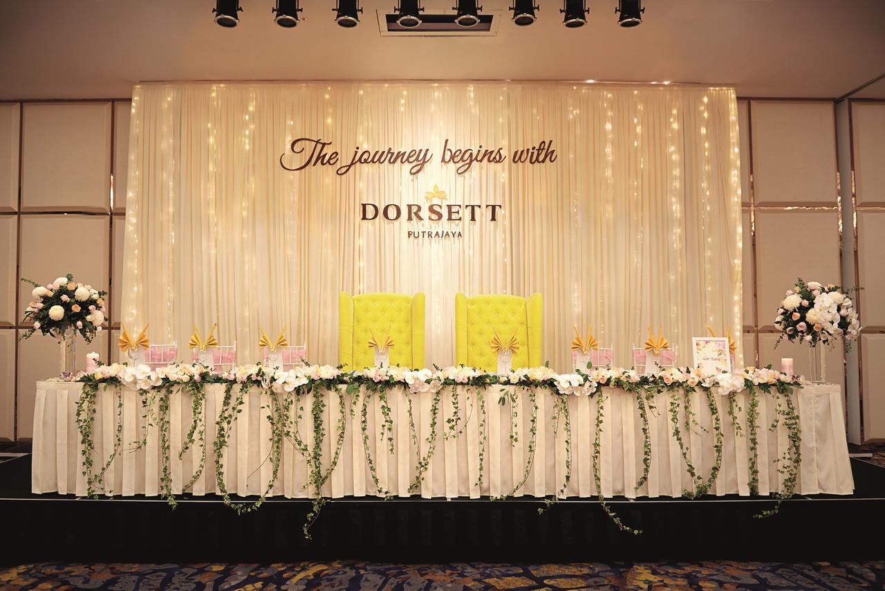 Hotel Dorsett Putrajaya Exteriér fotografie The photo depicts a decorated event space, likely set up for a celebration or ceremony. In the center, there is a backdrop with the phrase "The journey begins with DORSETT" prominently displayed. The backdrop is adorned with elegant draping and soft 