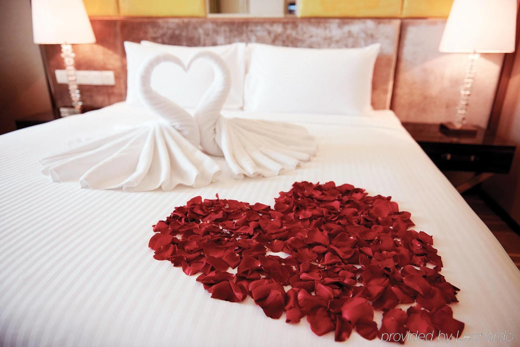 Hotel Dorsett Putrajaya Exteriér fotografie The photo shows a beautifully arranged bed with white bedding. On the bed, there is a decorative figure made from towels shaped like two swans forming a heart. Surrounding this figure is a heart made of red rose petals, adding a romantic touch to the