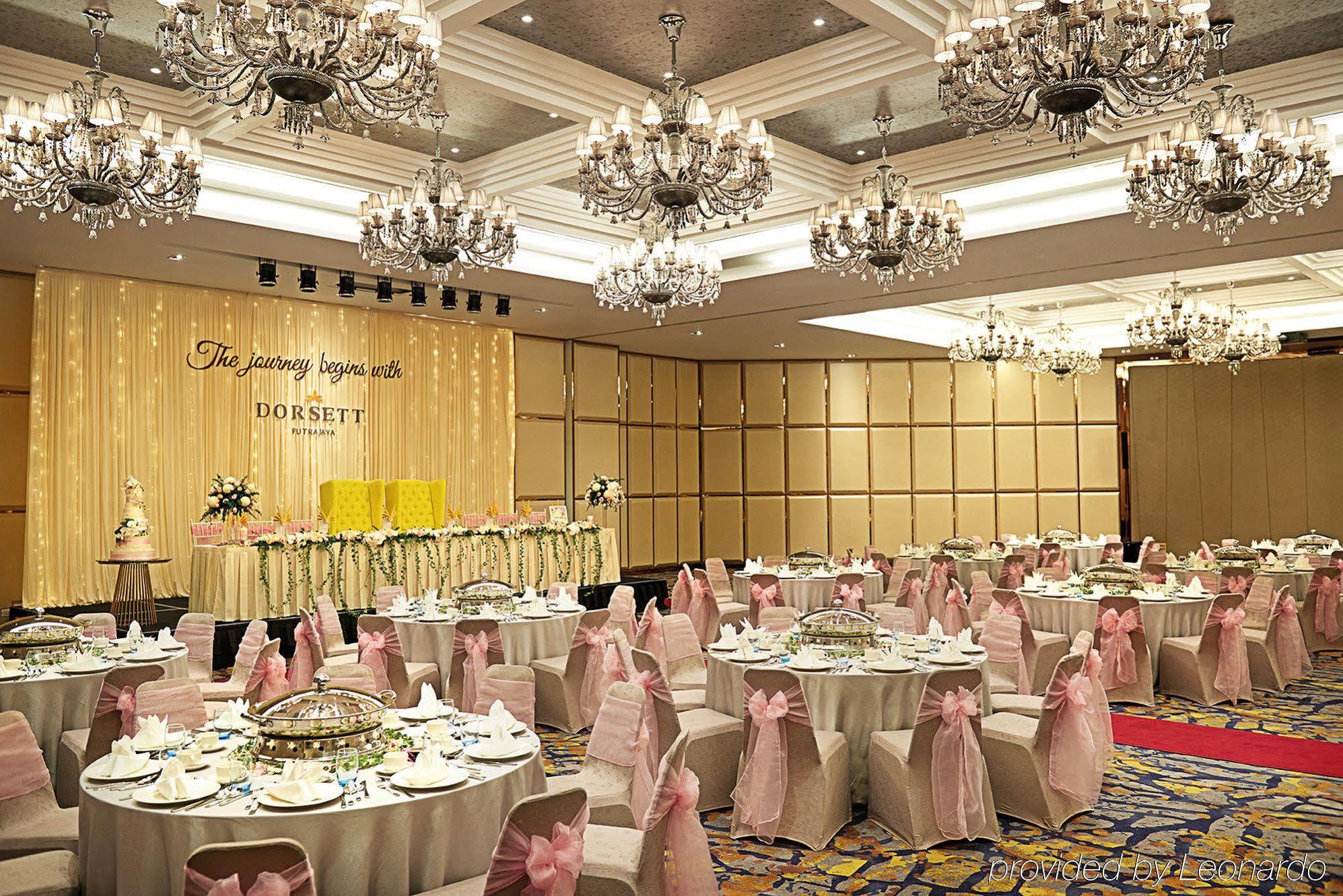 Hotel Dorsett Putrajaya Exteriér fotografie The photo shows an elegant banquet hall set up for a celebration or event. The room features numerous round tables covered with white tablecloths and adorned with pink sashes on the chairs. There are decorative centerpieces on the tables, and the wal