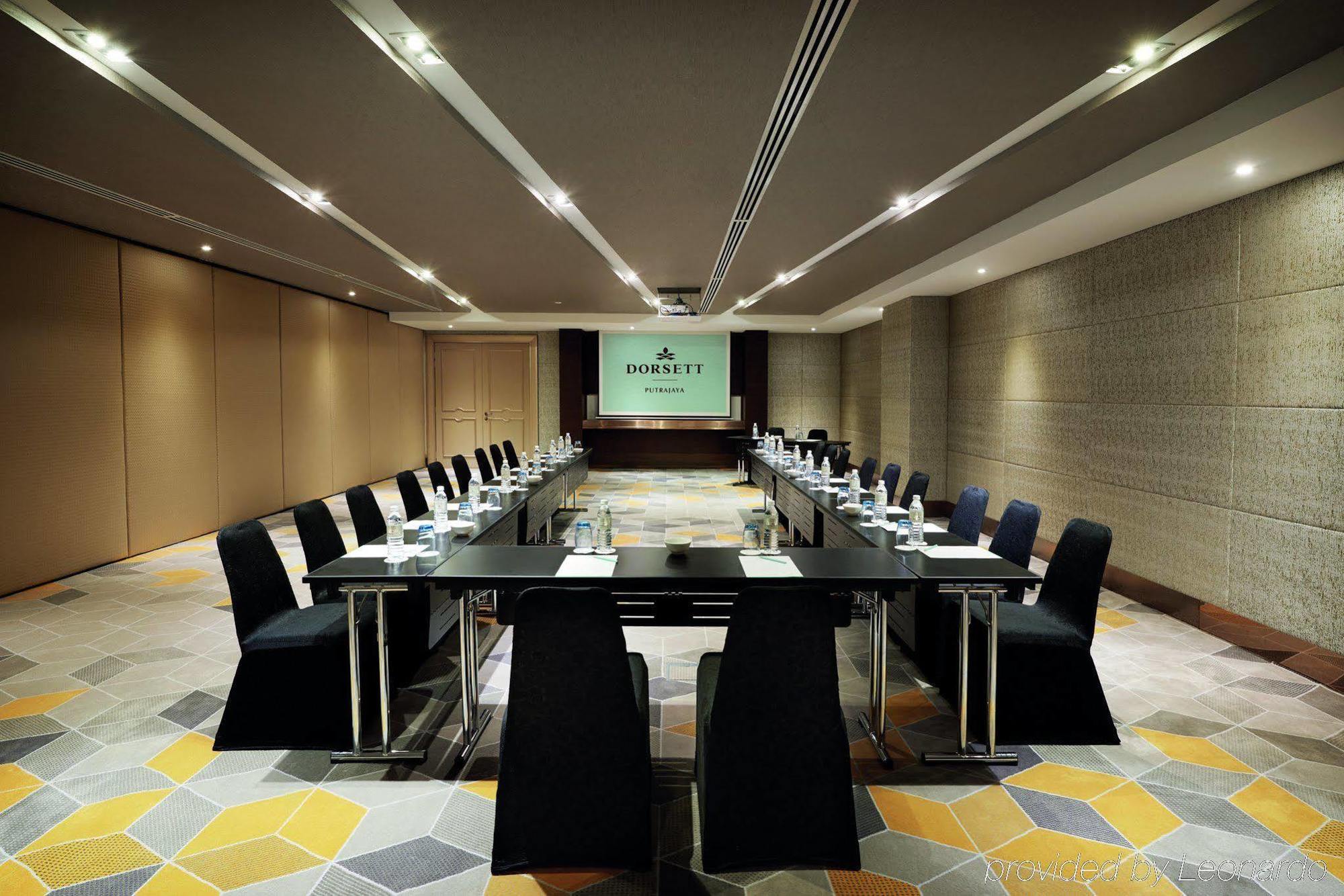 Hotel Dorsett Putrajaya Exteriér fotografie The photo shows a modern conference room arranged for a meeting. In the center, there is a large rectangular table surrounded by sleek black chairs. At the front of the room, there's a presentation screen with the name or logo displayed. The walls ar