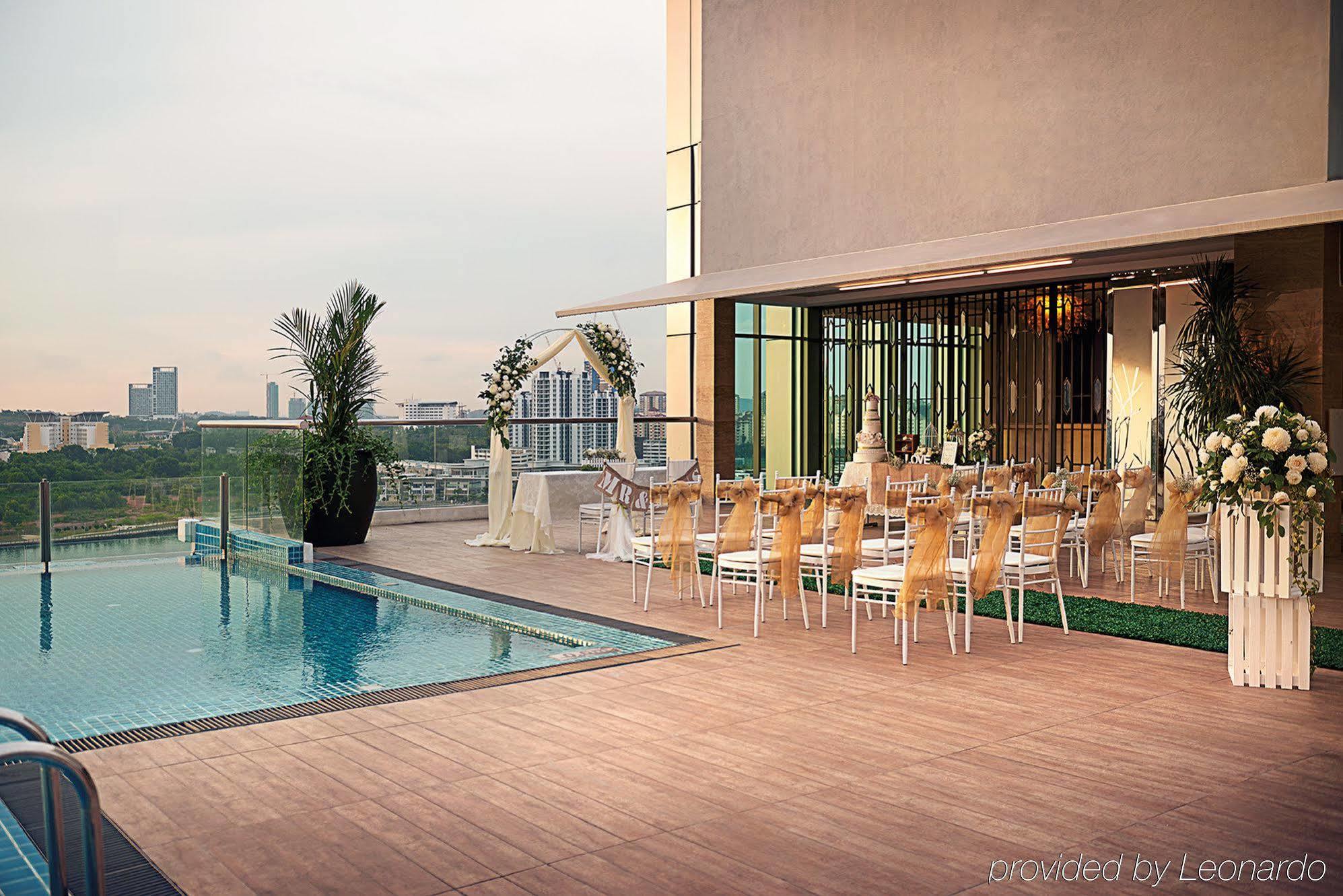 Hotel Dorsett Putrajaya Exteriér fotografie The photo shows an outdoor area featuring a swimming pool adjacent to a spacious terrace. On the terrace, there are several elegantly arranged tables and chairs, suggesting it is set up for an event, possibly a wedding or a formal gathering. The back