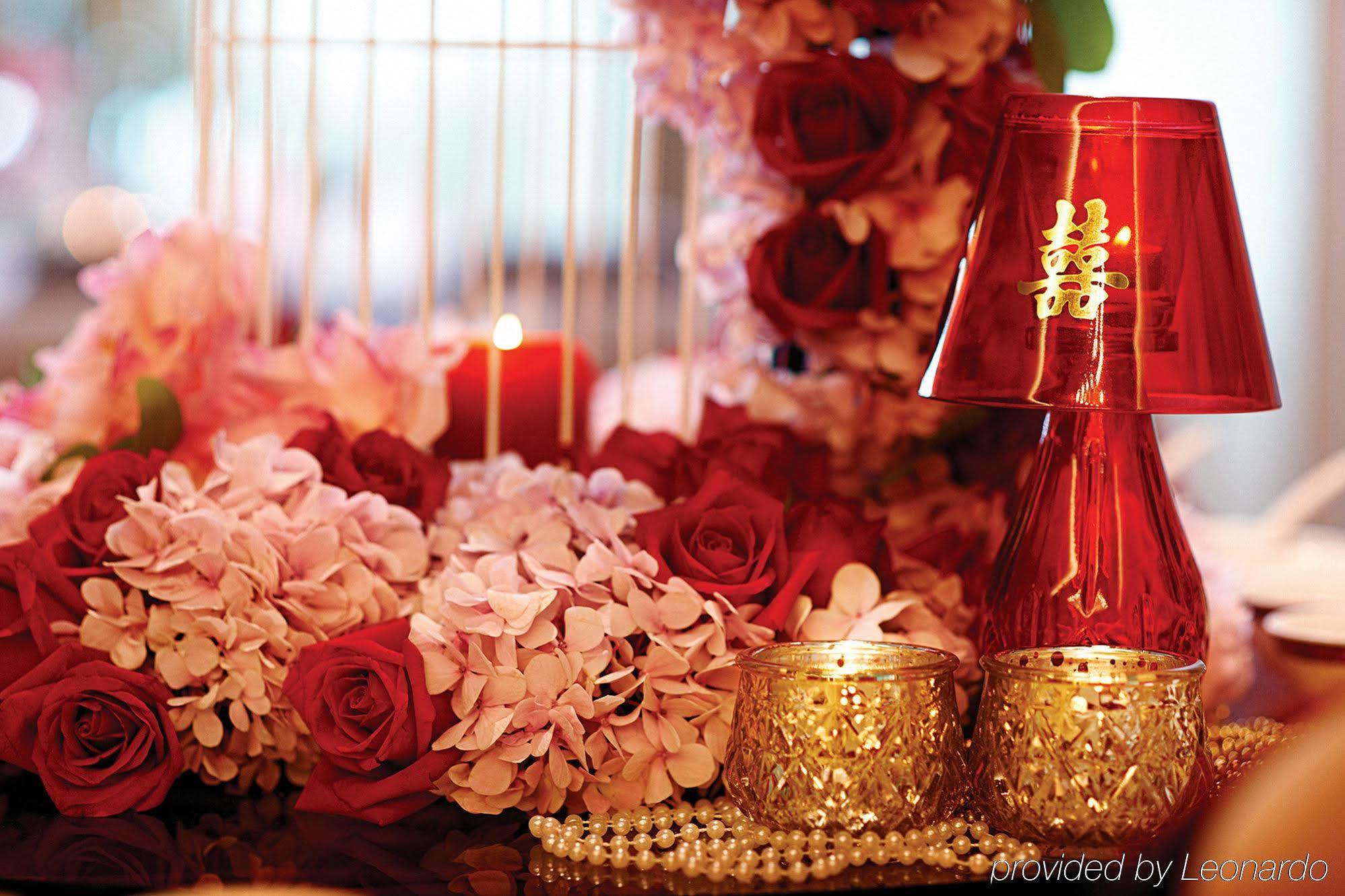 Hotel Dorsett Putrajaya Exteriér fotografie The photo features a beautiful arrangement that includes a mix of floral elements such as pink and red roses, along with other delicate flowers. In the center, there are decorative items like a shiny red vase or lamp with a traditional symbol on it, 