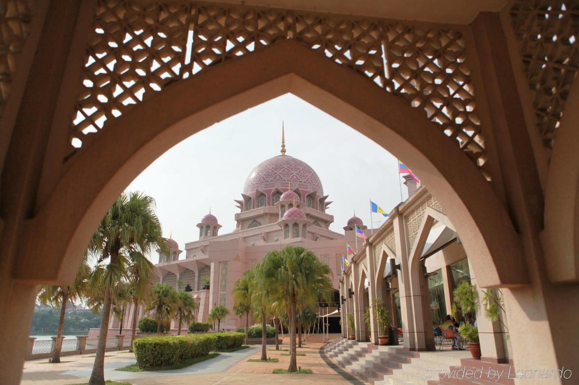 Hotel Dorsett Putrajaya Exteriér fotografie The photo shows an impressive architectural structure, likely a mosque, characterized by its pink dome and ornate design. The building features multiple domes and minarets. In the foreground, there is a beautifully crafted archway with intricate latt