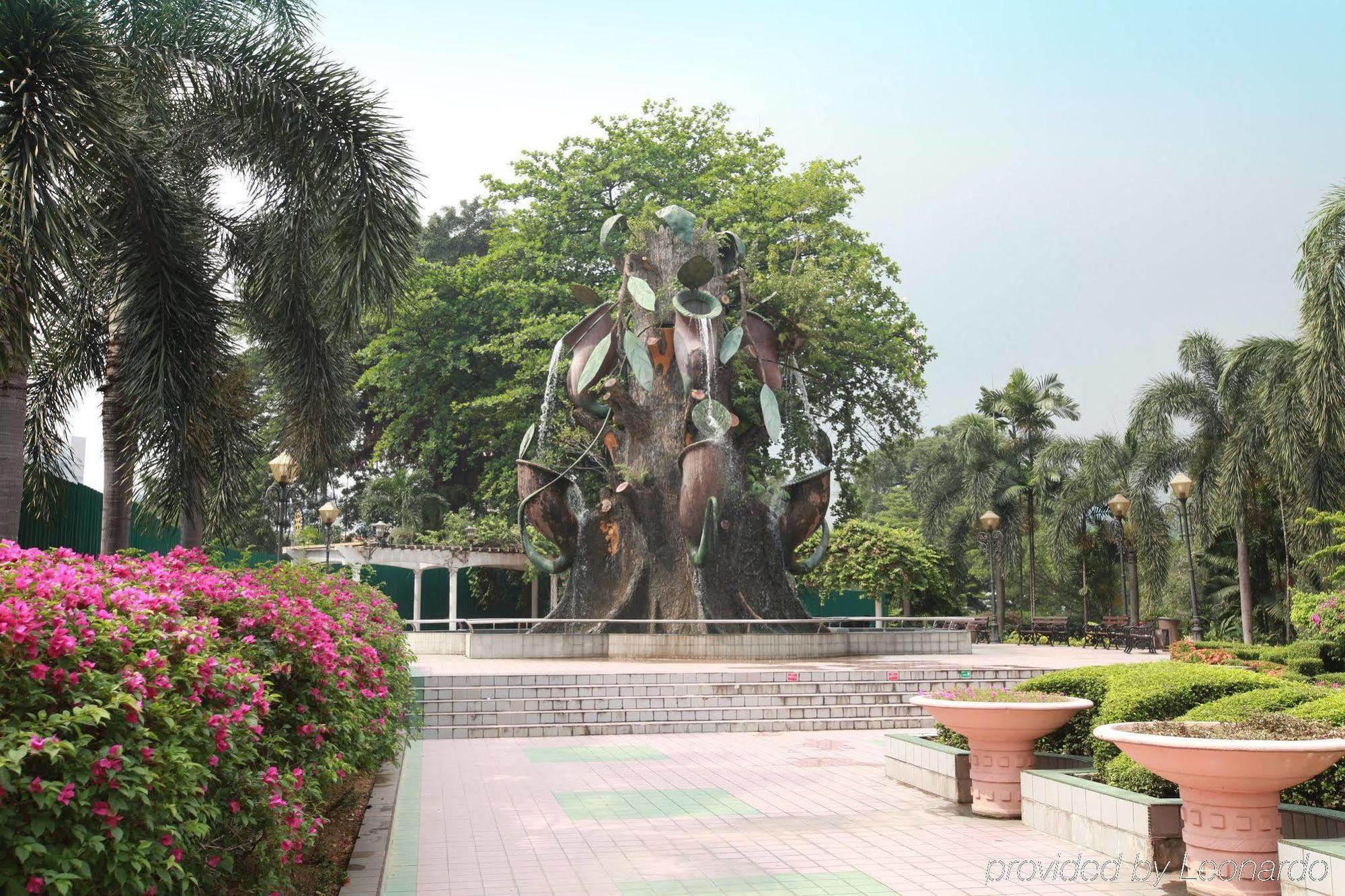 Hotel Dorsett Putrajaya Exteriér fotografie The photo shows a park setting featuring a large, artistic water fountain that resembles a stylized tree or plant. The fountain has metallic and leafy elements, giving it a unique and modern appearance. Surrounding the fountain are lush green trees a