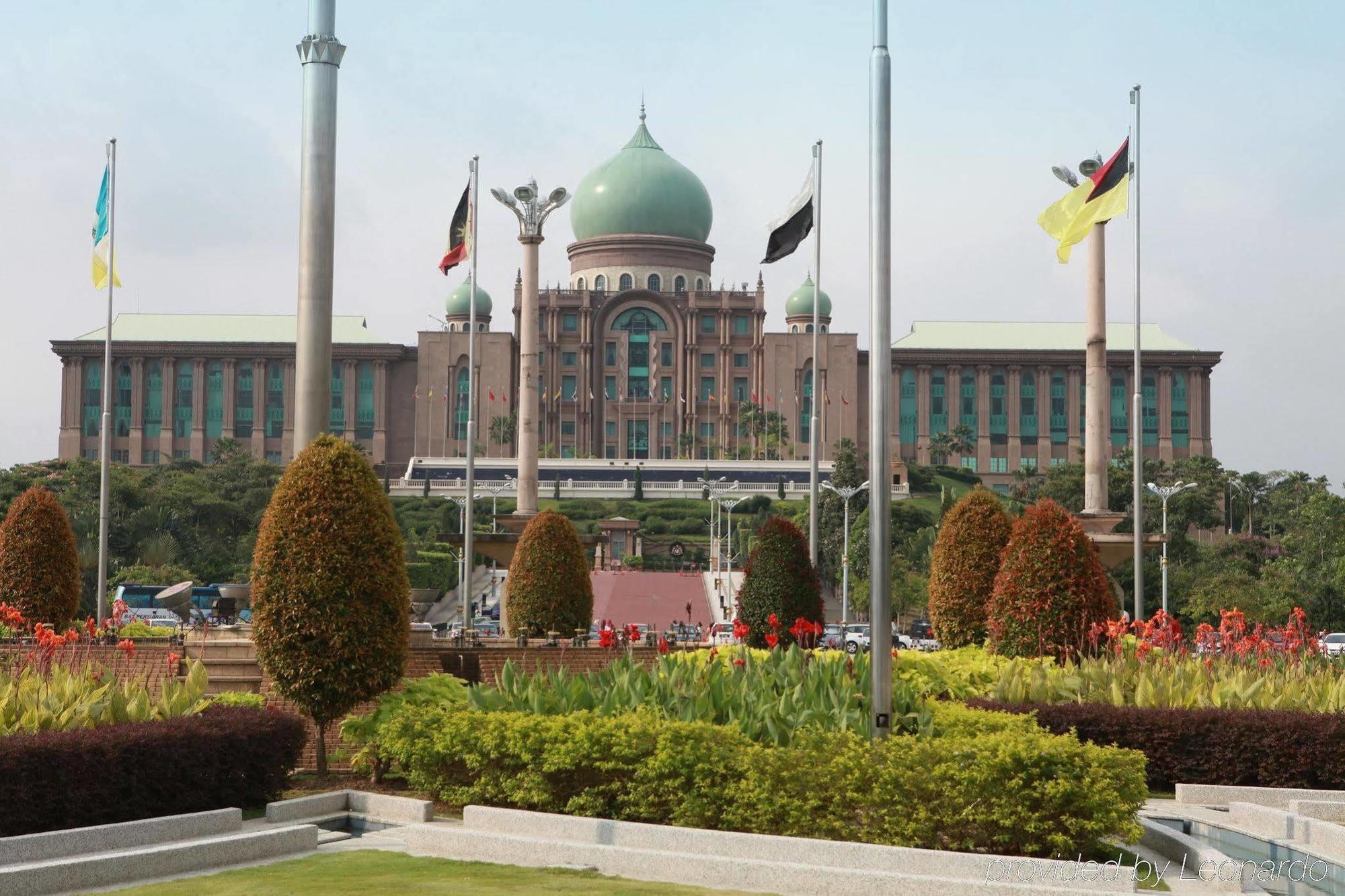 Hotel Dorsett Putrajaya Exteriér fotografie The photo depicts a large, impressive building with a distinctive dome at the top. This structure is likely surrounded by well-maintained gardens featuring various plants and flowers. In the foreground, there are neatly arranged flower beds and bushe