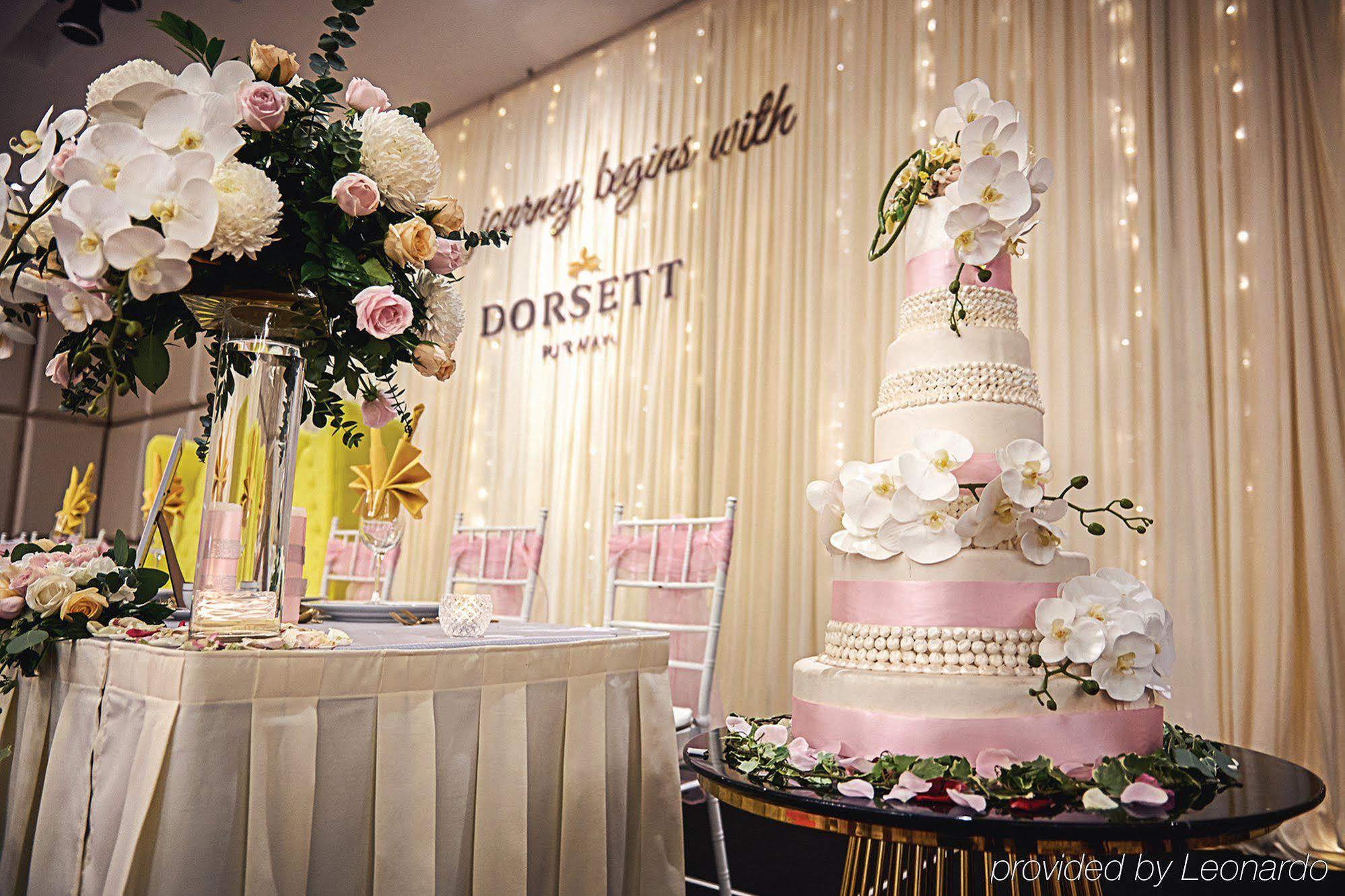 Hotel Dorsett Putrajaya Exteriér fotografie The photo shows a beautifully decorated event space, likely for a wedding or special celebration. On the left, there is a tall floral arrangement featuring white orchids and pink roses, placed on a glass pedestal. The arrangement adds an elegant touc