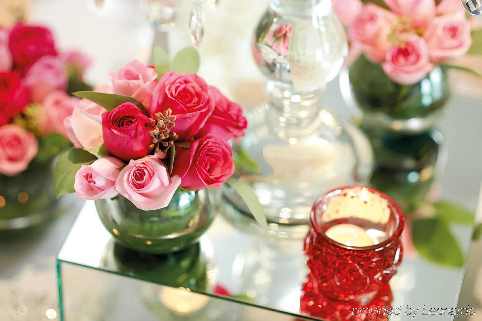 Hotel Dorsett Putrajaya Exteriér fotografie The photo features a decorative arrangement of flowers. There are mixed pink roses in a small glass vase, alongside a few green leaves for contrast. The flowers are arranged attractively, and there are additional floral arrangements in the background