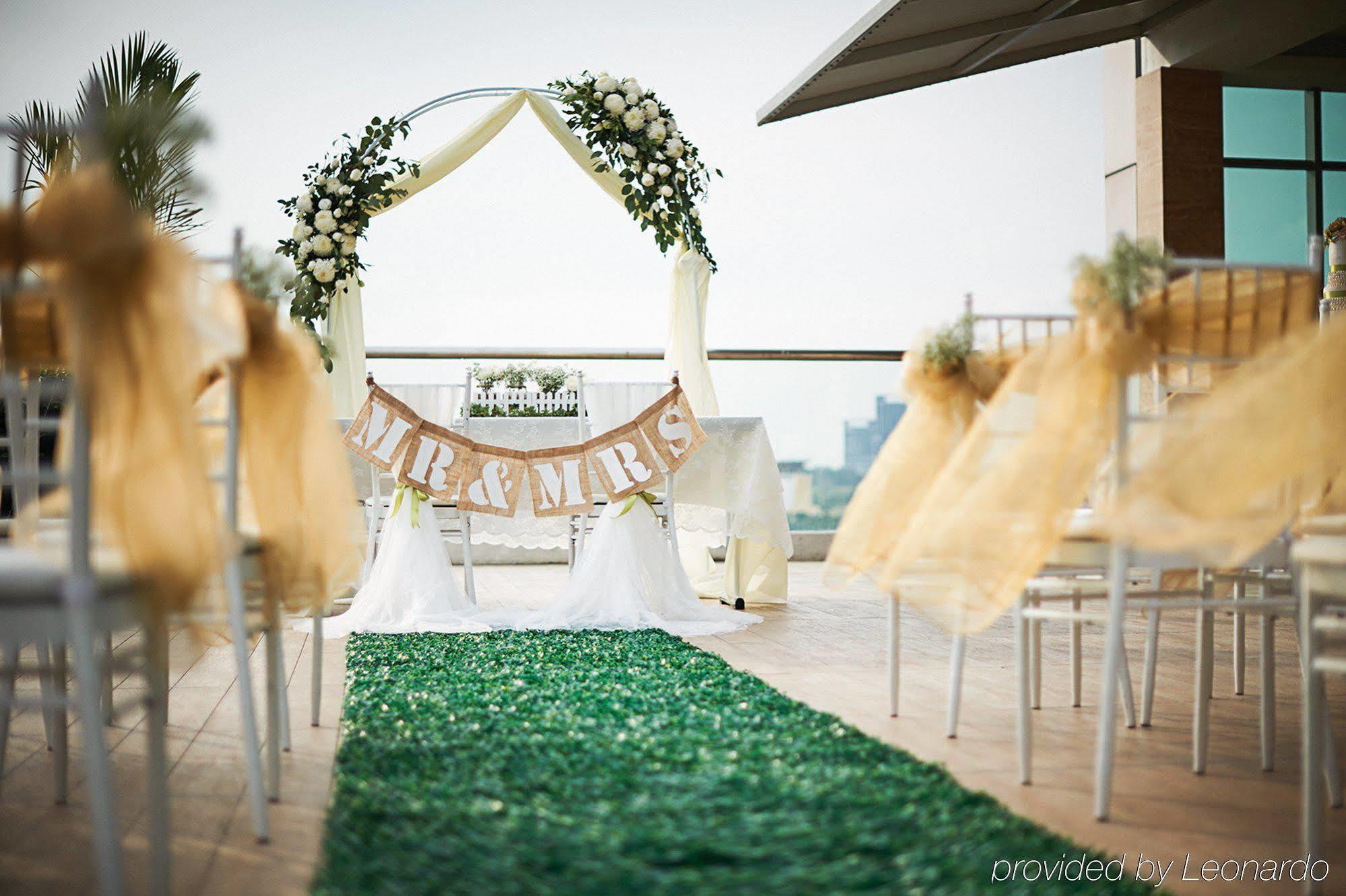 Hotel Dorsett Putrajaya Exteriér fotografie The photo depicts a beautifully arranged outdoor wedding setting. In the foreground, there is a green carpet leading to an altar or archway adorned with flowers and draped fabric. Above the altar, a banner reads "MR & MRS," indicating it is a wedding