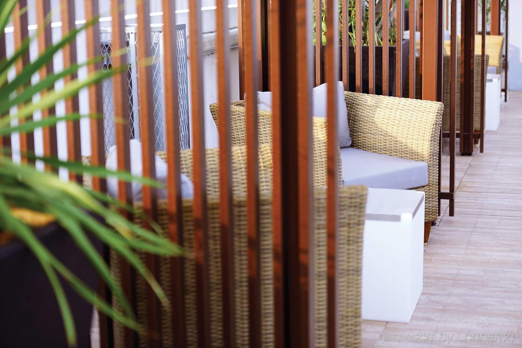 Hotel Dorsett Putrajaya Exteriér fotografie The photo shows a cozy outdoor seating area. There are two wicker chairs with gray cushions positioned near a small white table. The seating is partially surrounded by wooden slats, which create a sense of privacy and separation from the rest of the 