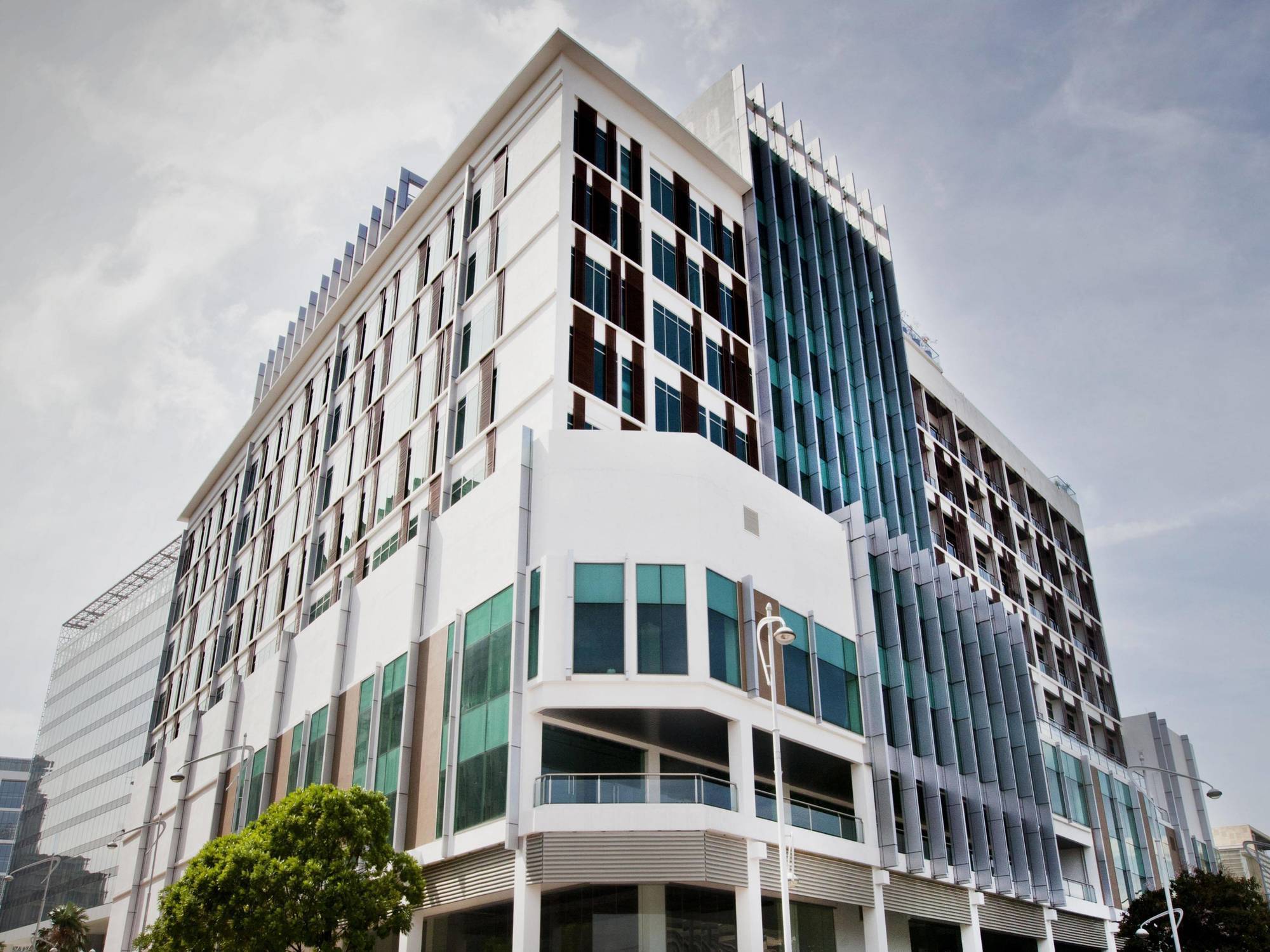 Hotel Dorsett Putrajaya Exteriér fotografie The photo shows a modern multi-story building with a contemporary architectural design. The structure features a combination of large glass windows and white panels, giving it a sleek appearance. The building has multiple levels, with a prominent gla